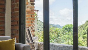 Una habitación con sofá y hamaca, ventanas amplias con vistas a zonas verdes y montañas.