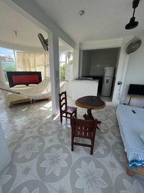 A room with a bed, a dining table with chairs, a hammock, and a kitchenette.