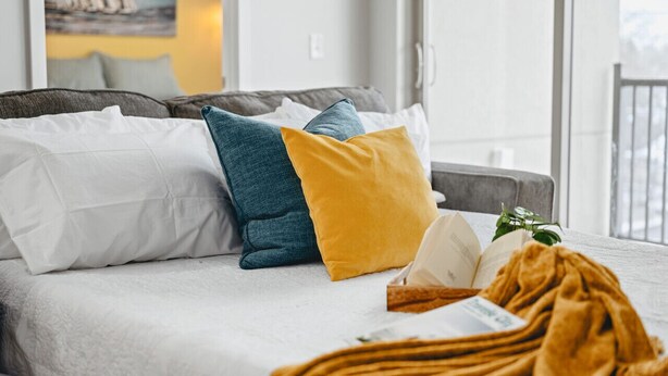 Una cama con varias almohadas, una manta y un libro.