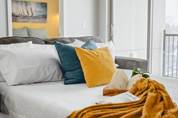 A bed with multiple pillows, a blanket, and a book. - Shoreline 2BR Condo Near Downtown The Bay and Wineries (Traverse City)