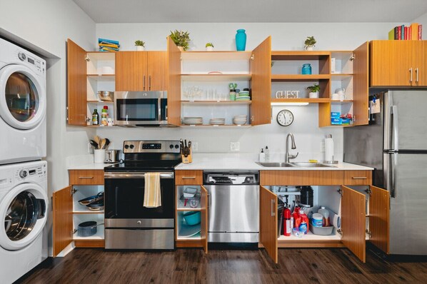 Una cocina compacta con electrodomésticos integrados, armarios de madera y estanterías abiertas.