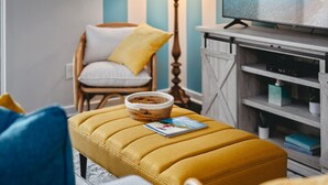 A living room with a yellow ottoman, a wicker basket, and a television on a wooden stand.
