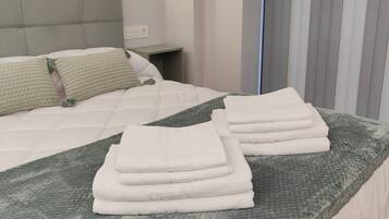 Una cama bien hecha con una colcha gris y toallas blancas dobladas, un cabecero, una mesita de noche y una pared con un diseño circular decorativo.