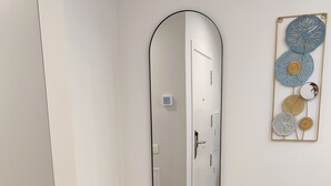 A room with a large oval mirror, a tufted bench, and a teal armchair. - Loft Moderno, Céntrico y Acogedor (Oviedo)