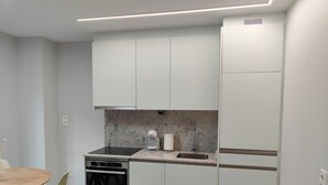 A modern kitchen with white cabinets, a black countertop, a built-in oven, and a refrigerator. - Loft Moderno, Céntrico y Acogedor (Oviedo)