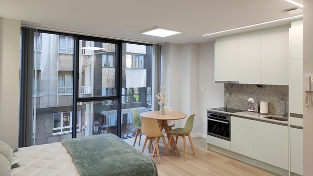 A modern apartment with a large window, a dining area, and a kitchenette. - Loft Moderno, Céntrico y Acogedor (Oviedo)