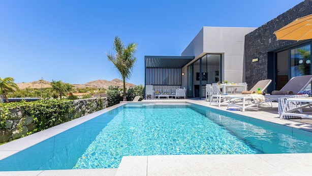 Un área de piscina moderna con una piscina azul cristalina, sillas de descanso y una mesa con sillas.