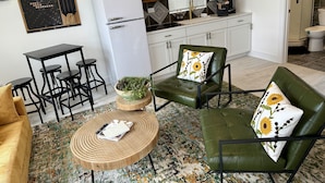 Un espace de vie compact comprenant un coin cuisine, un coin repas et un espace détente avec un canapé vert et une table ronde en bois.