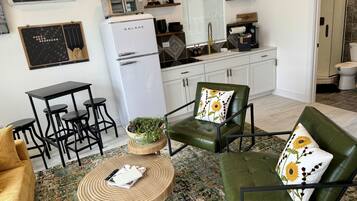 Un espace de vie compact comprenant un coin cuisine, un coin repas et un espace détente avec un canapé vert et une table ronde en bois.