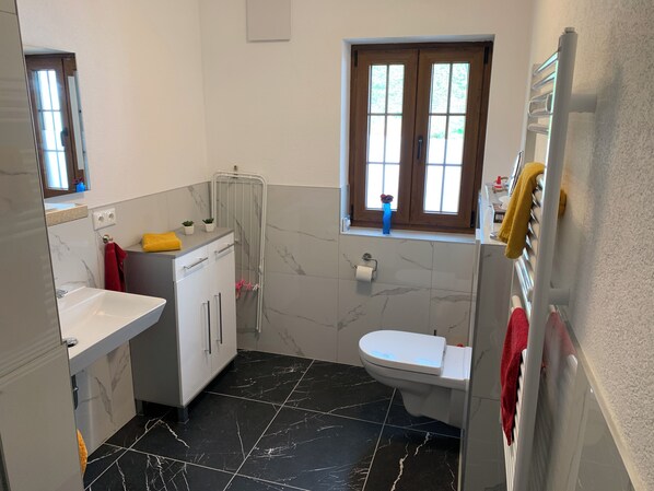 A bathroom with a white sink, a toilet, and a window with wooden shutters.