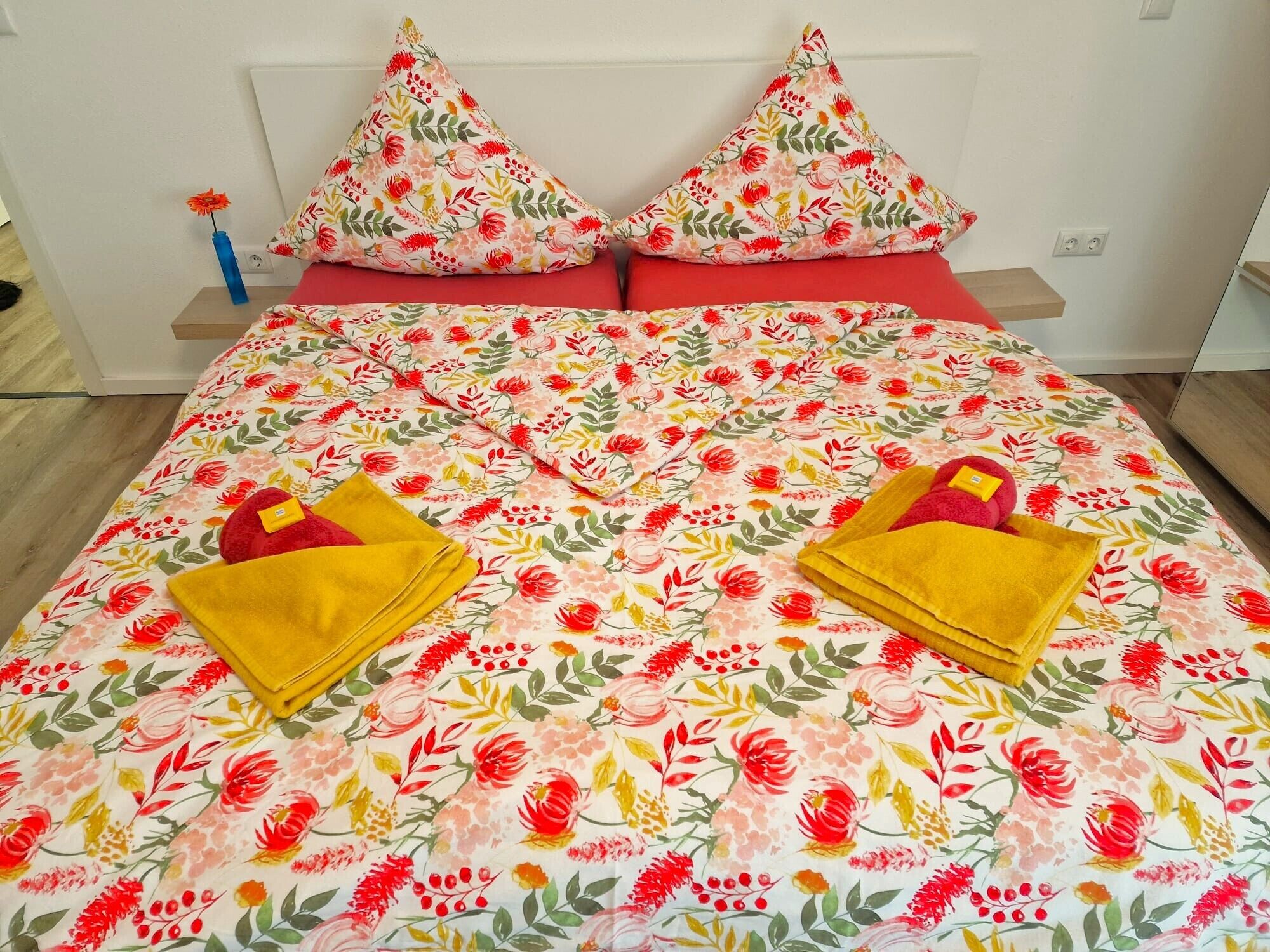 Una cama con ropa de cama floral, dos almohadas y dos toallas dobladas.