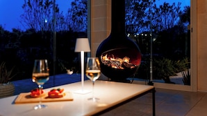 A modern outdoor dining area with a glass table, two wine glasses, and a fire feature. - Villa Belkis 6, Emma Villas (Ostuni)