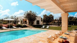 A poolside area with a table set for dining, lounge chairs, and a pergola structure. - Villa Belkis 6, Emma Villas (Ostuni)