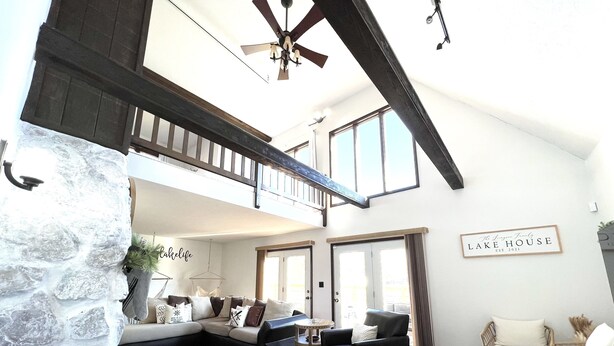 A spacious living area with a stone wall, a black leather sofa, a black leather chair, and a white armchair. There is a sign on the wall that reads "Lake House". - Life-Giving, Quiet retreat only 25 min west of Indpls. Peace, Pace, & Gratitude (Coatesville)