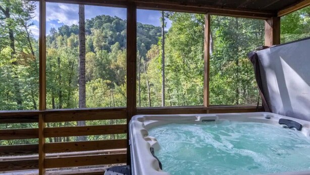 Un jacuzzi con vistas a un bosque a través de amplios ventanales.