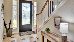 Un vestíbulo con una puerta negra, una escalera de madera, un tapete, una planta en maceta y una lámpara.