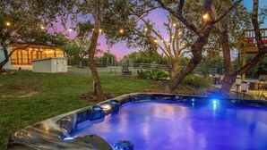 Un jacuzzi en un patio trasero con una casa y árboles al fondo.