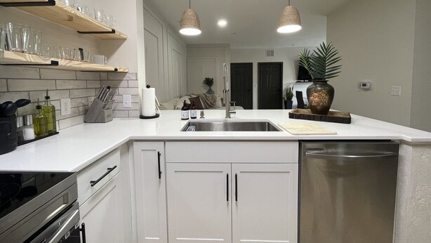 Een moderne keuken met witte kasten, een roestvrijstalen spoelbak en hangende lampen.