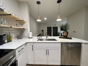 Een moderne keuken met witte kasten, een roestvrijstalen spoelbak en hangende lampen.
