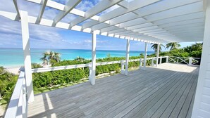 Ein Holzdeck mit weißer Reling, das auf einen Strand und den Ozean blickt.