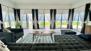 Ein geräumiges Wohnzimmer mit großem Fenster und Meerblick, ausgestattet mit einer Couch, einem Sessel und einem Couchtisch.