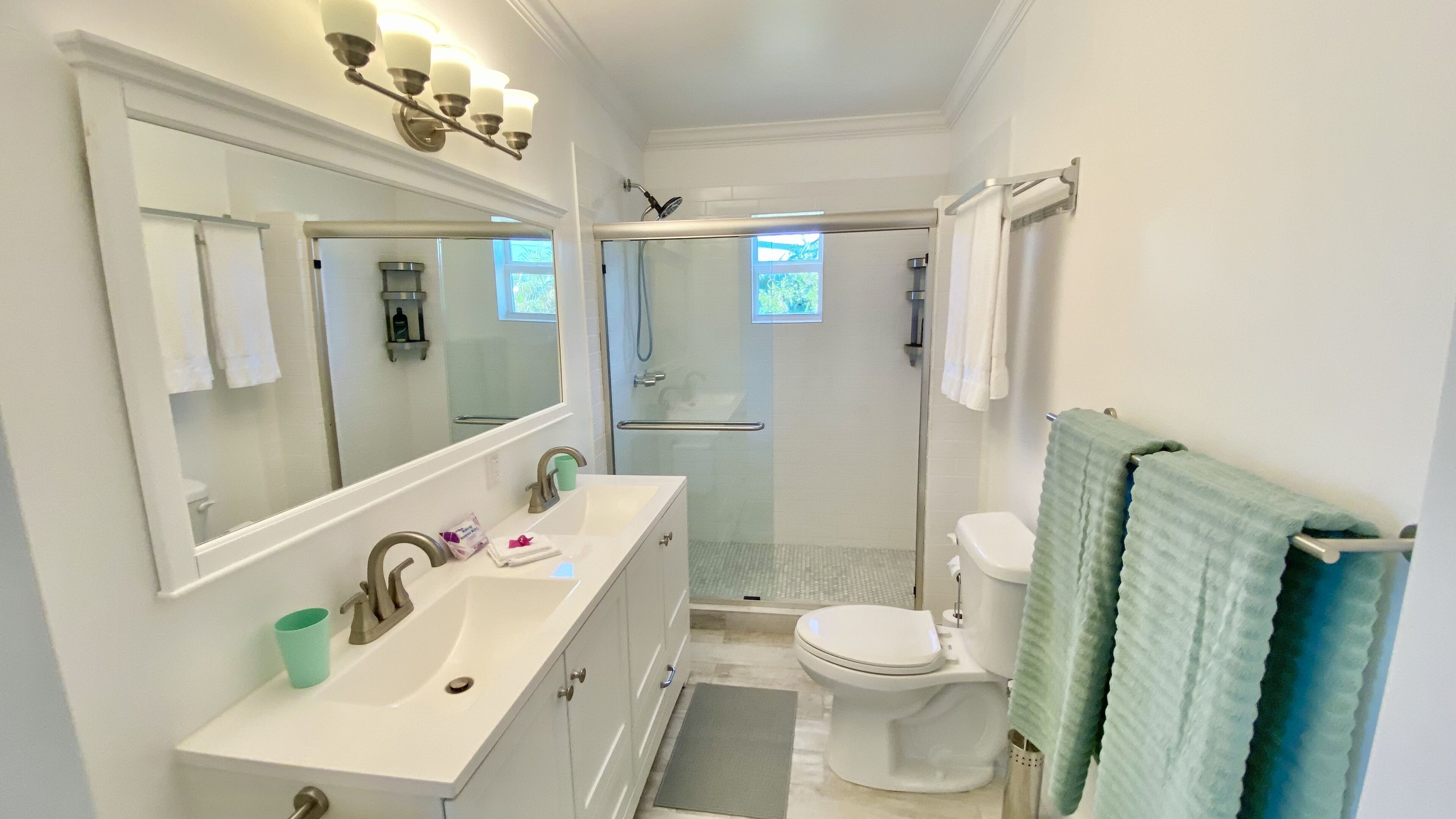 Une salle de bain moderne avec un grand miroir, deux lavabos, une douche et des toilettes.