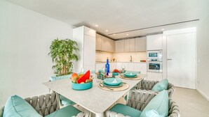 A modern kitchen with white cabinets, a dining table with teal chairs, and a potted plant.