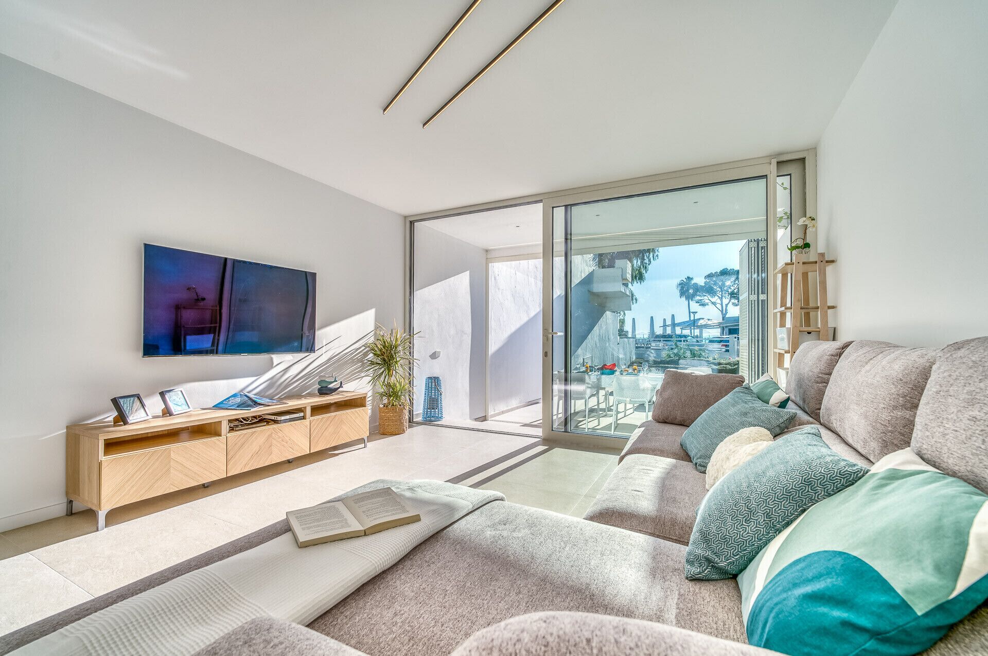 En moderne stue med sofa, sofabord, fjernsyn og en skydedør, der fører til en balkon.