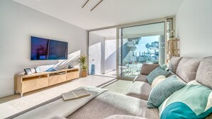 A modern living room with a sofa, a coffee table, a TV, and a sliding glass door leading to a balcony.