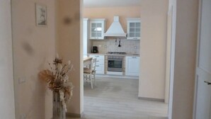 Une cuisine avec des meubles blancs, un îlot central et un coin repas avec une chaise.