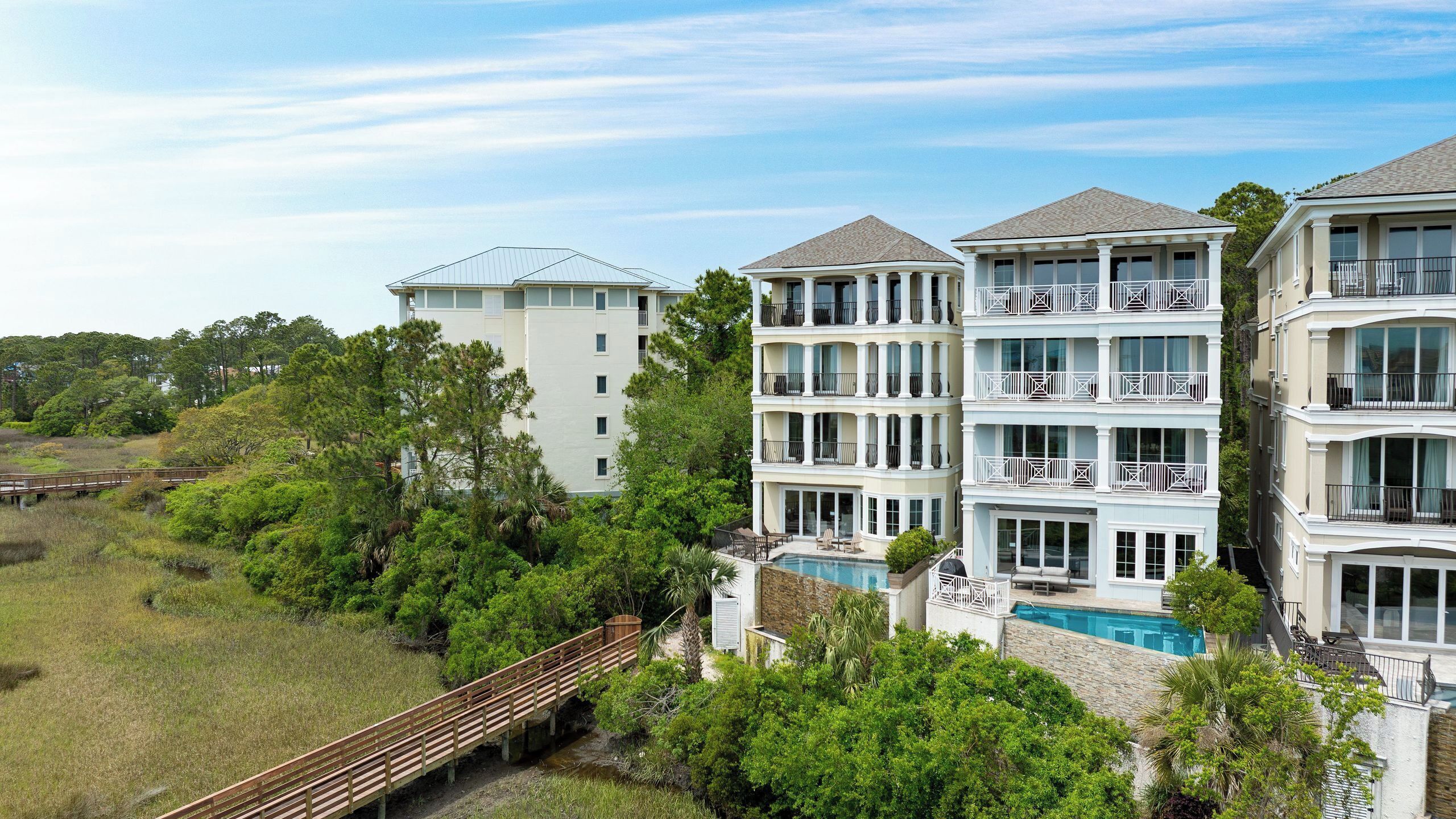 A multi-story hotel with a pool, surrounded by greenery and a wooden bridge.