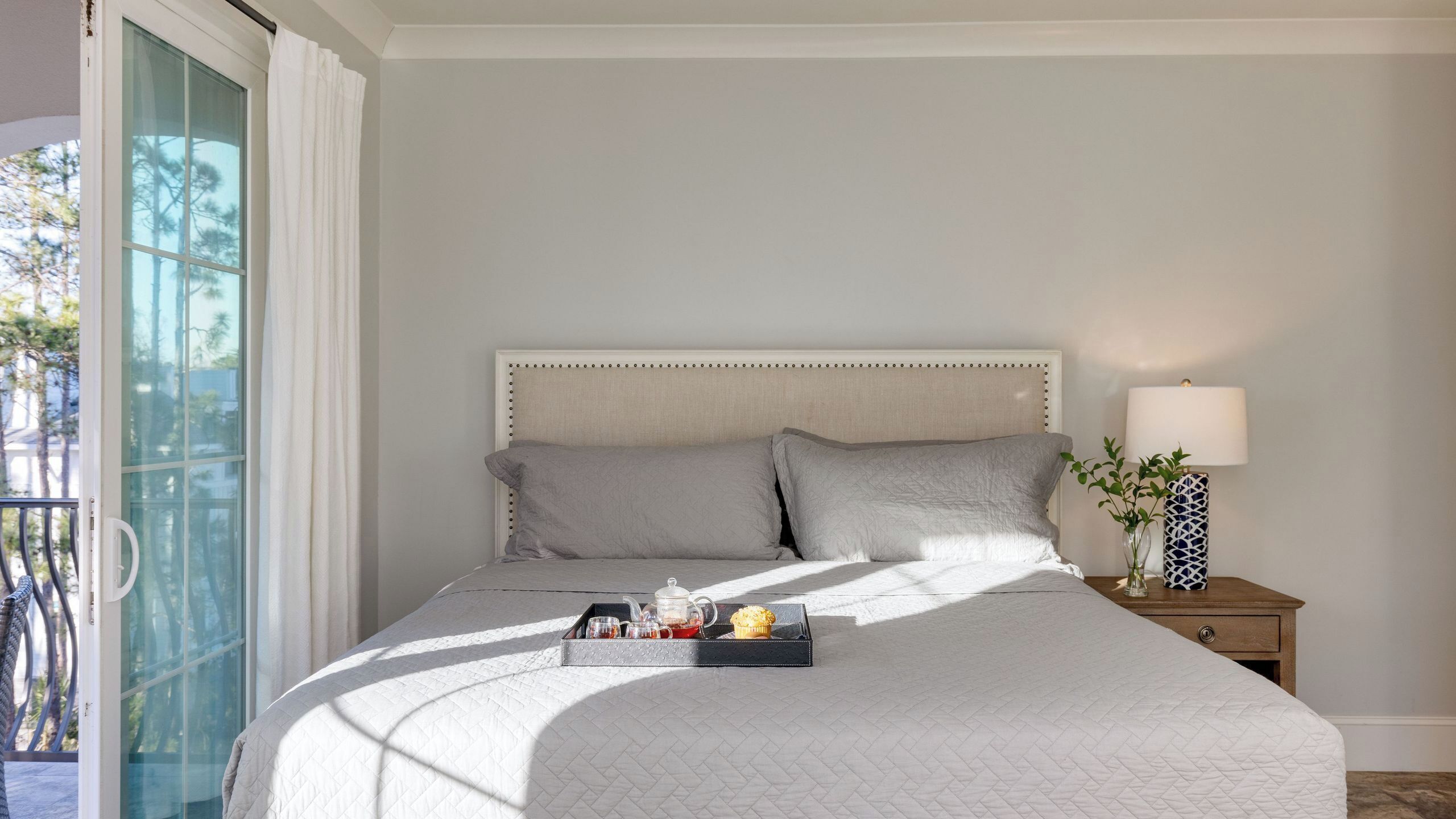 A bedroom with a bed, a bedside table with a lamp, and a tray with a teapot and muffin.