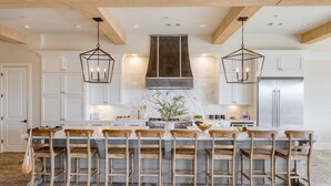 Une cuisine dotée d’un grand îlot central, de chaises en bois et de luminaires suspendus.