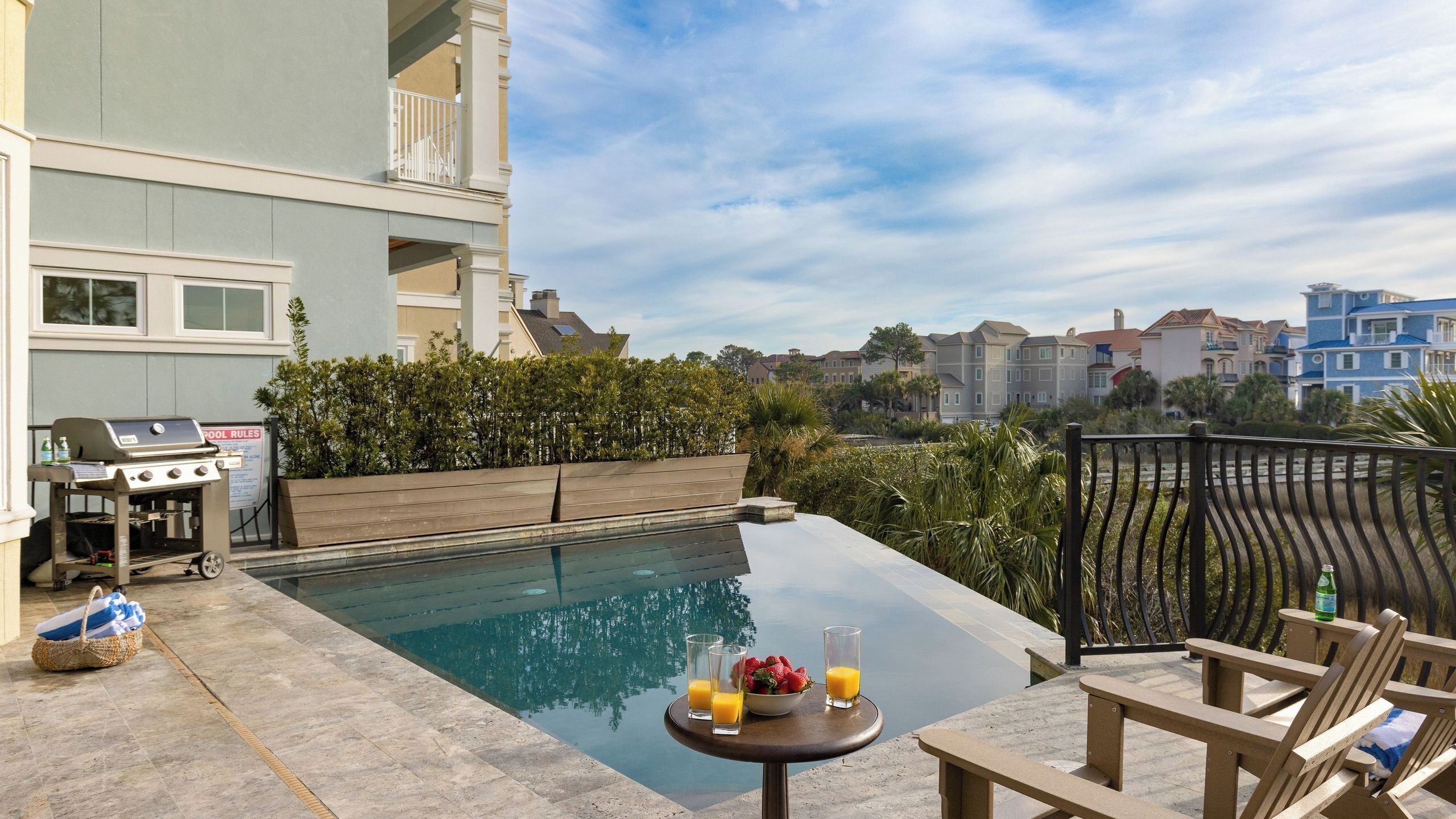Une piscine sur le toit, avec un barbecue, des chaises longues et une table où sont disposés des fruits et des boissons.
