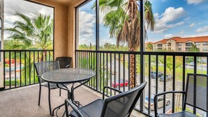 A balcony with a round table and chairs, large windows with a view of palm trees and a parking lot. - Awesome Vacation Destination! 1304 Tuscana Resort (Davenport)