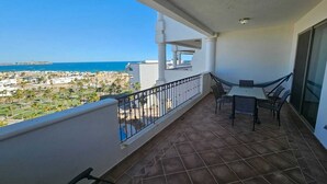 Un balcón con mesa y sillas, vista al mar y suelo de baldosas.