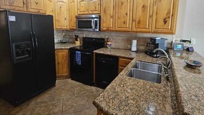 Una cocina con armarios de madera, un refrigerador negro, microondas, estufa y encimeras de granito.