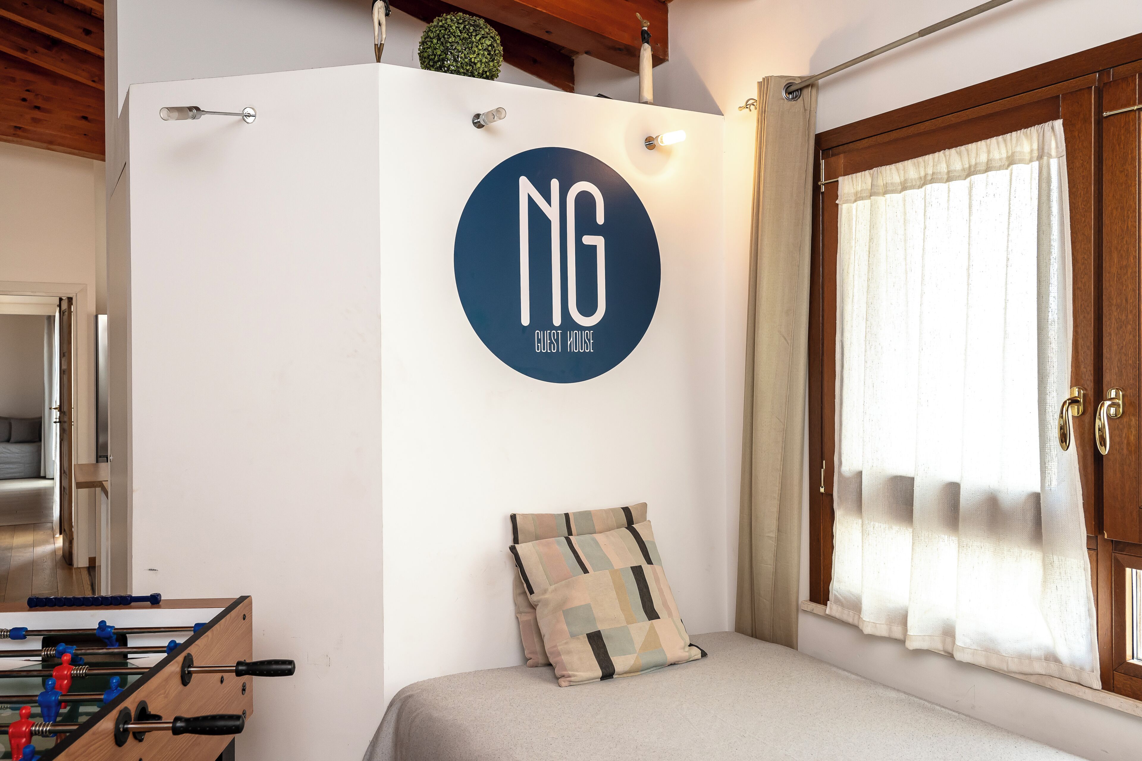 Una habitación con una cama, un logotipo en la pared, una ventana con cortinas, techo de madera y una puerta.