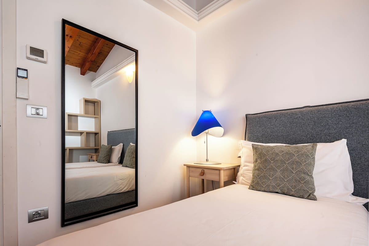 Quarto com cama, mesa de cabeceira, abajur, espelho e guarda-roupa.