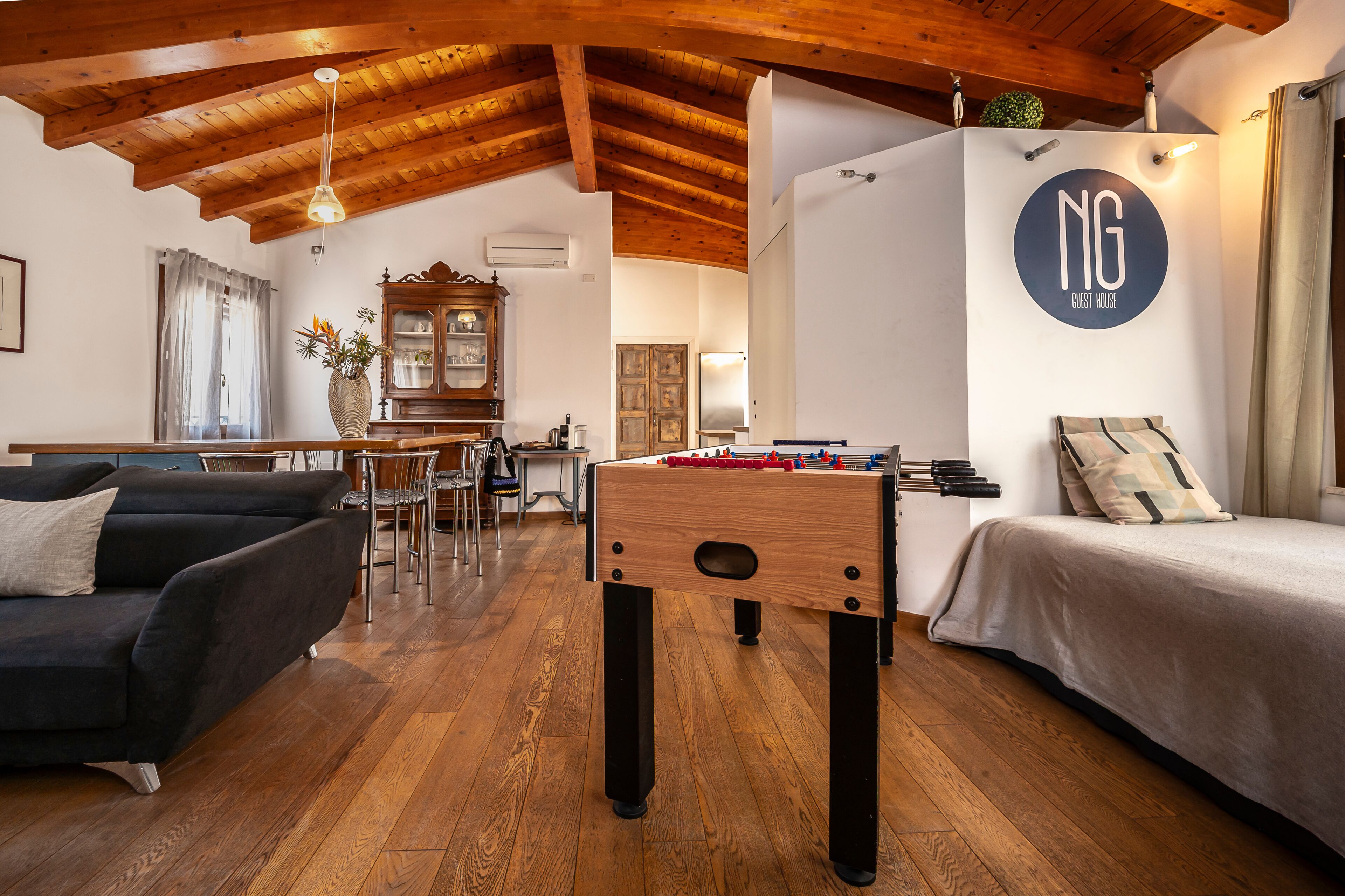A cozy room with a foosball table, a sofa, a bed, and a wooden ceiling.