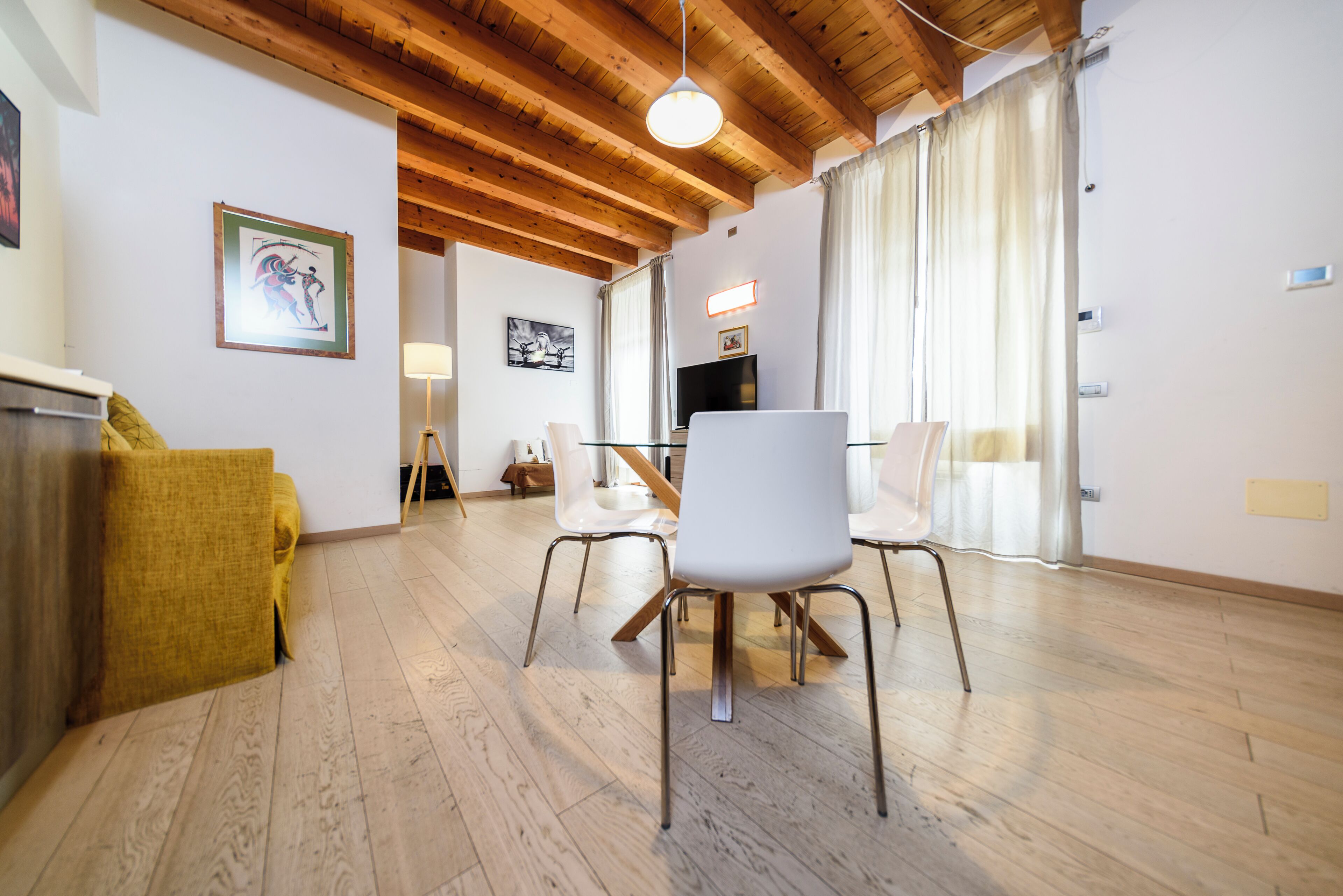 Una sala de estar moderna con techo de madera, una mesa de comedor con sillas, televisor y obras de arte en las paredes.