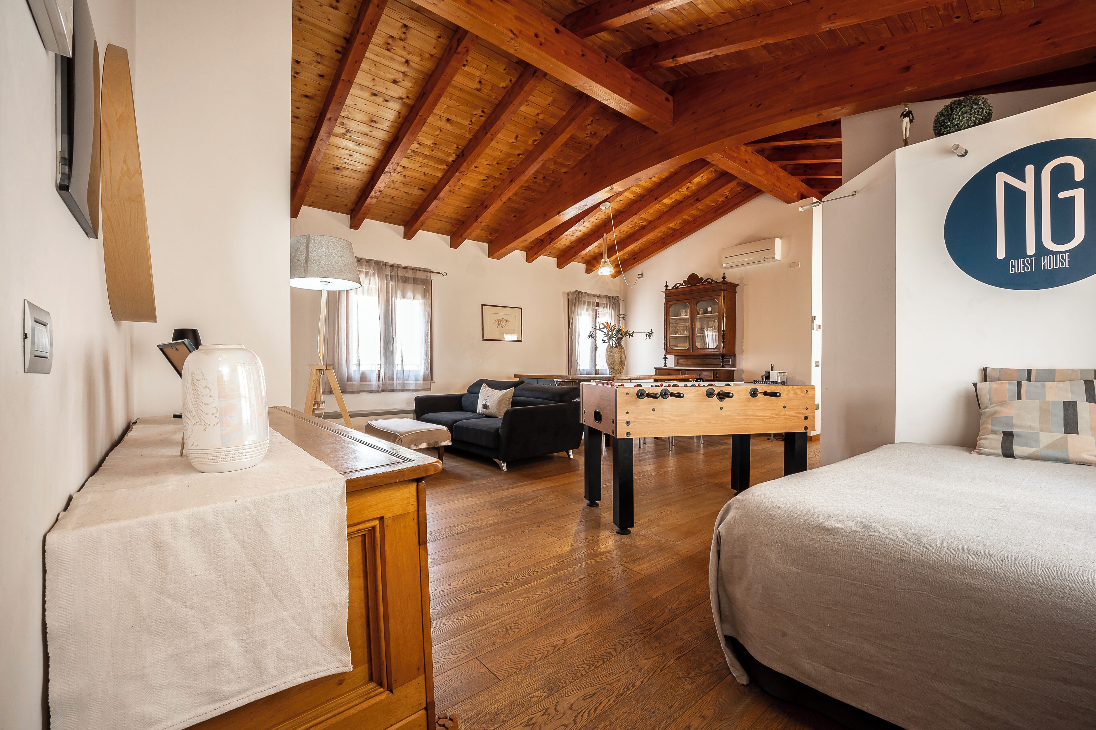Une pièce chaleureuse avec un plafond en bois, un lit, un canapé, une table de baby-foot et une pancarte indiquant « NG GUEST HOUSE ».