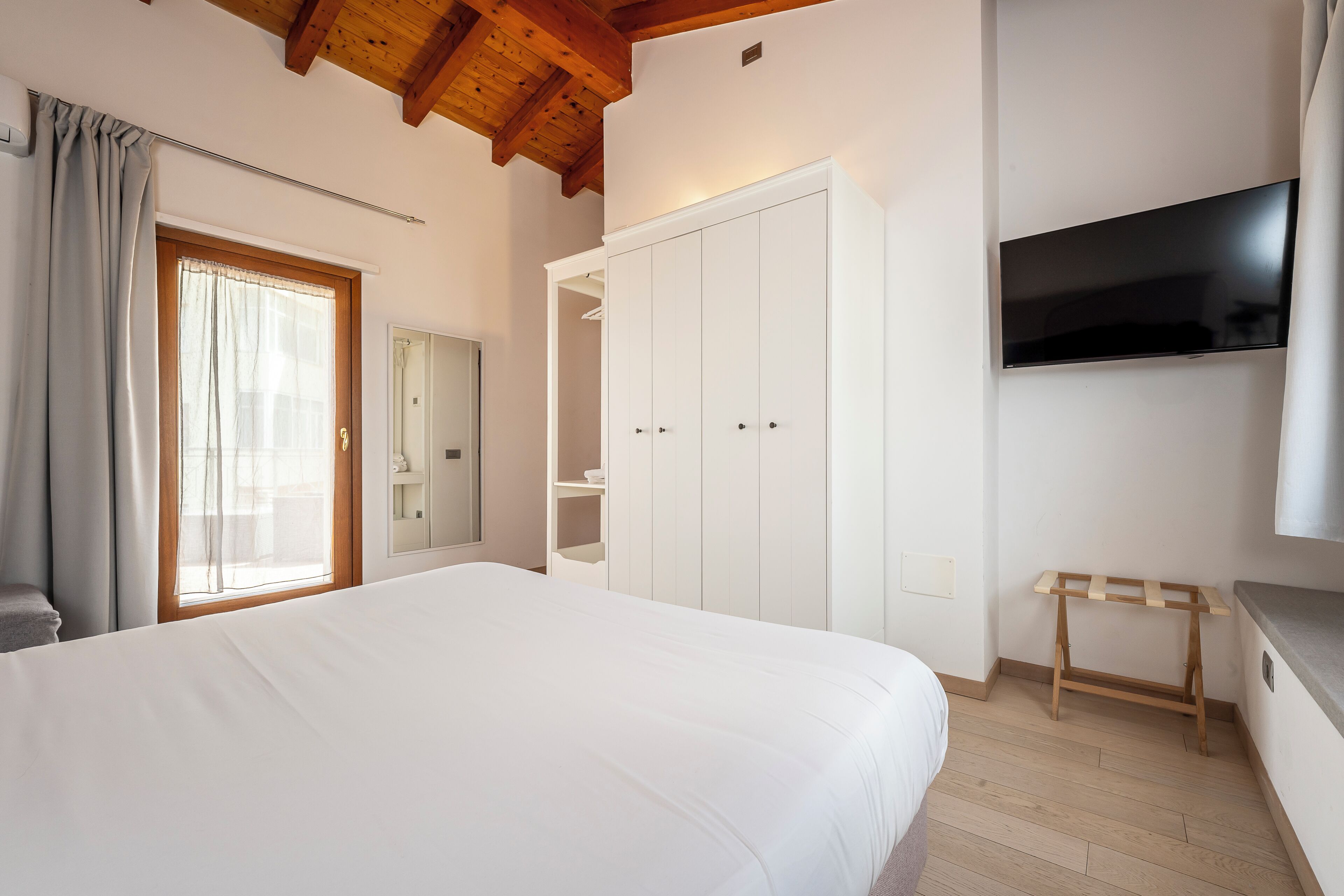 A bedroom with a bed, a wardrobe, a TV, and a wooden shelf.