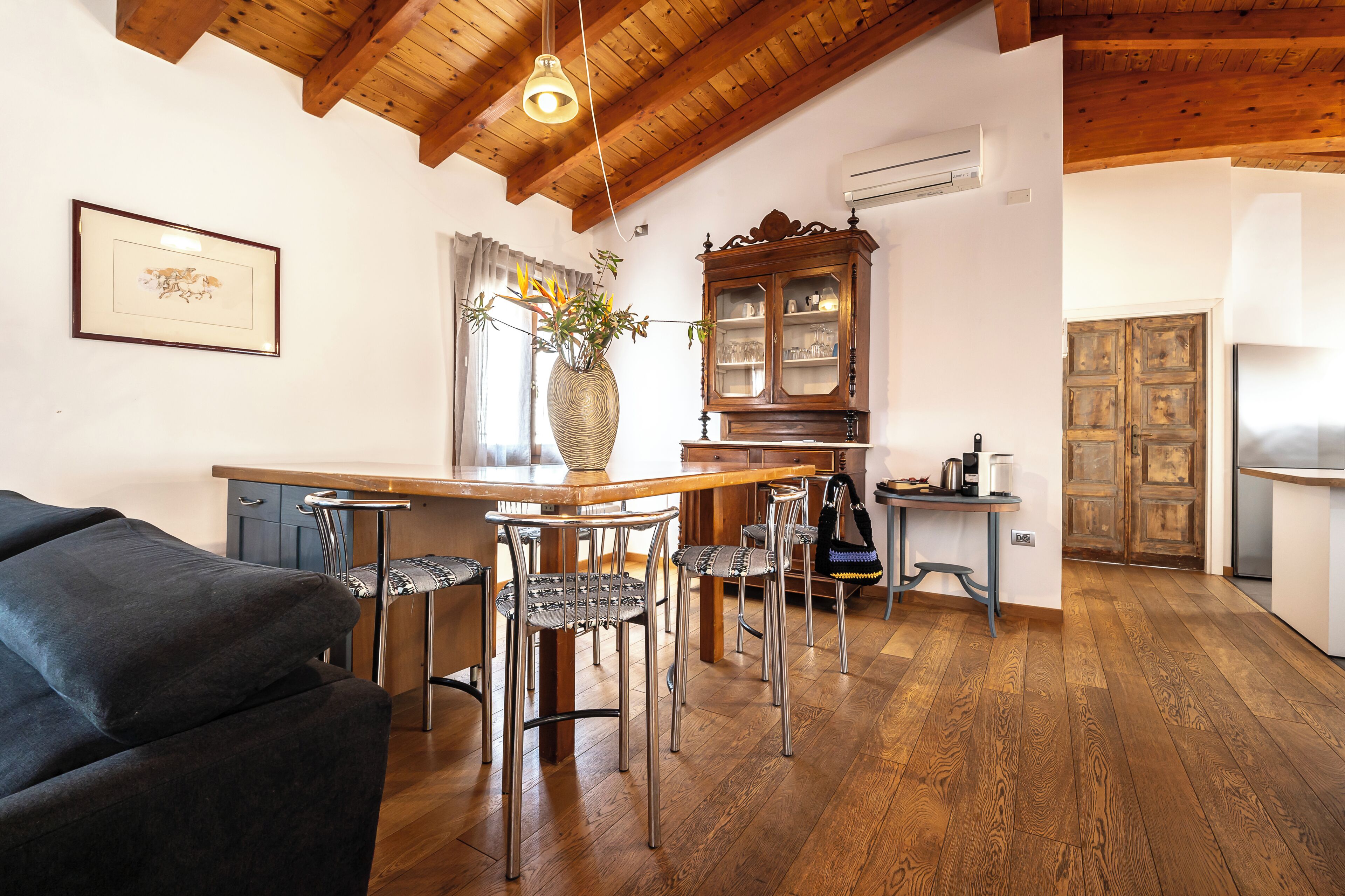A dining area with a wooden table, metal chairs, a vase with flowers, a cabinet, and a door.