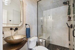 Ein modernes Badezimmer mit einem Waschbecken aus Glas, einer Toilette, einer Dusche und einem großen Spiegel.