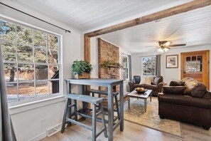 A cozy living room with a fireplace, a dining area with a bench, and a large window offering a view of the outdoors. - Blue Spruce Cabin (Allenspark)