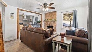 Un salon chaleureux avec une cheminée, un canapé en cuir marron, une table basse en bois et un ventilateur de plafond.