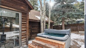 Een houten chalet met een jacuzzi en een glazen deur.