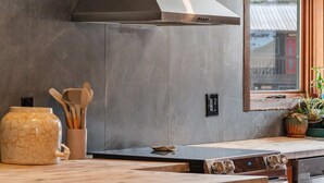 Een keuken met een groot eiland, een roestvrijstalen afzuigkap en een raam met uitzicht op een rood gebouw.
