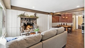 Ein gemütliches Wohnzimmer mit Kamin aus Stein, einer Couch und einem Essbereich mit Holztisch und Stühlen.